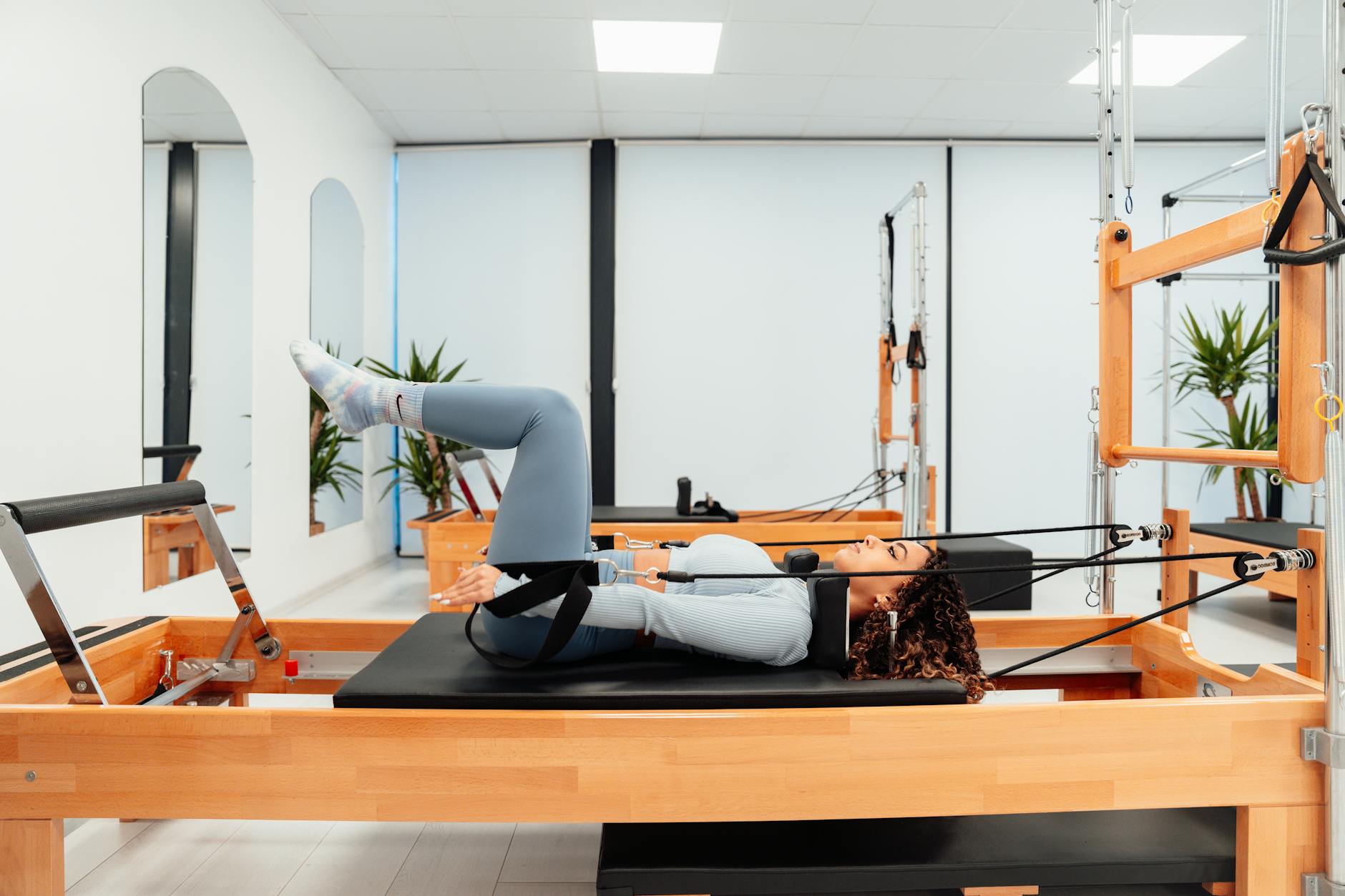 Kobieta ćwicząca pośladki na reformerze Pilates w nowoczesnej siłowni