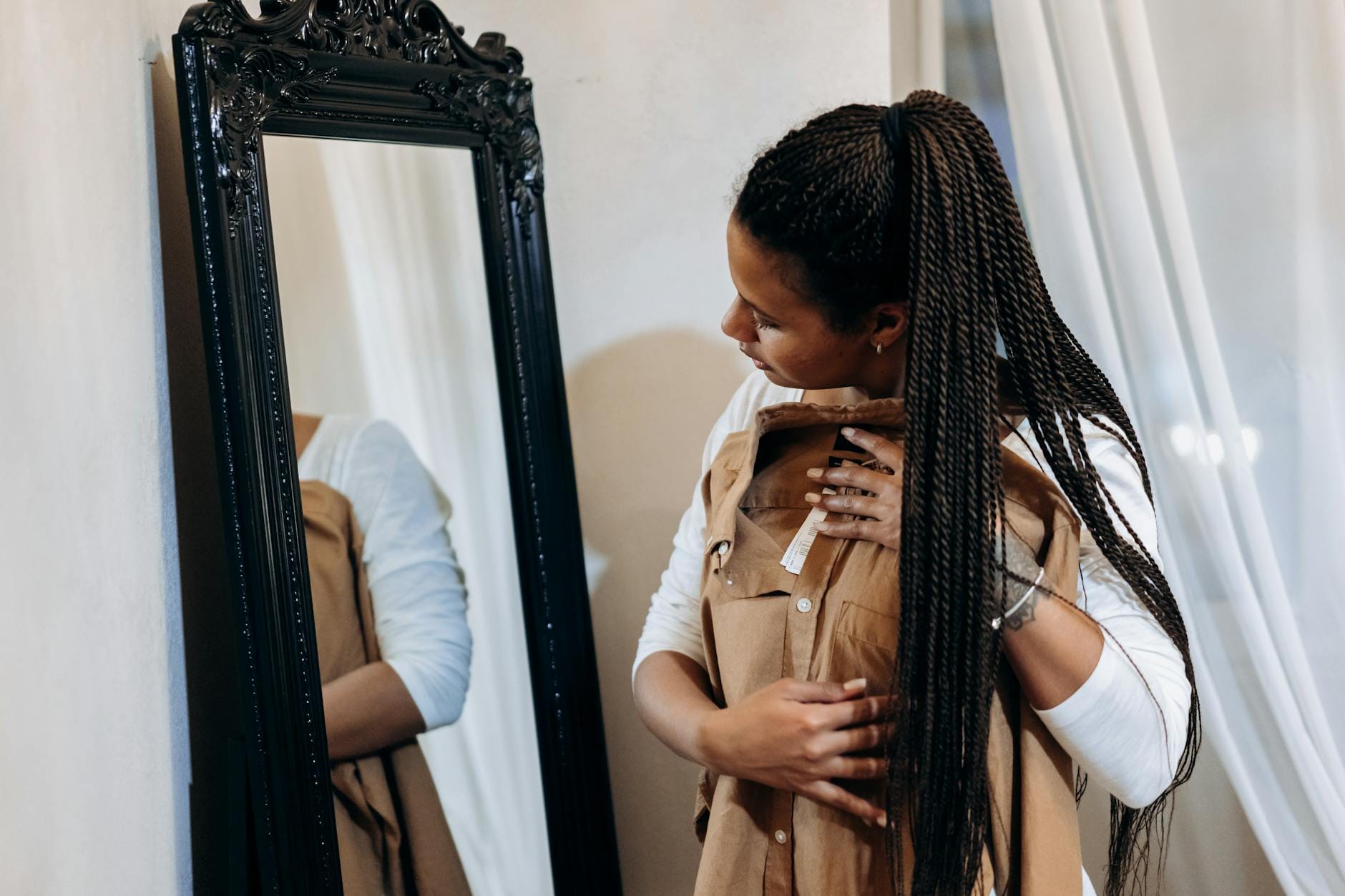 Kobieta z warkoczami ogląda sukienkę w lustrze w mieszkaniu