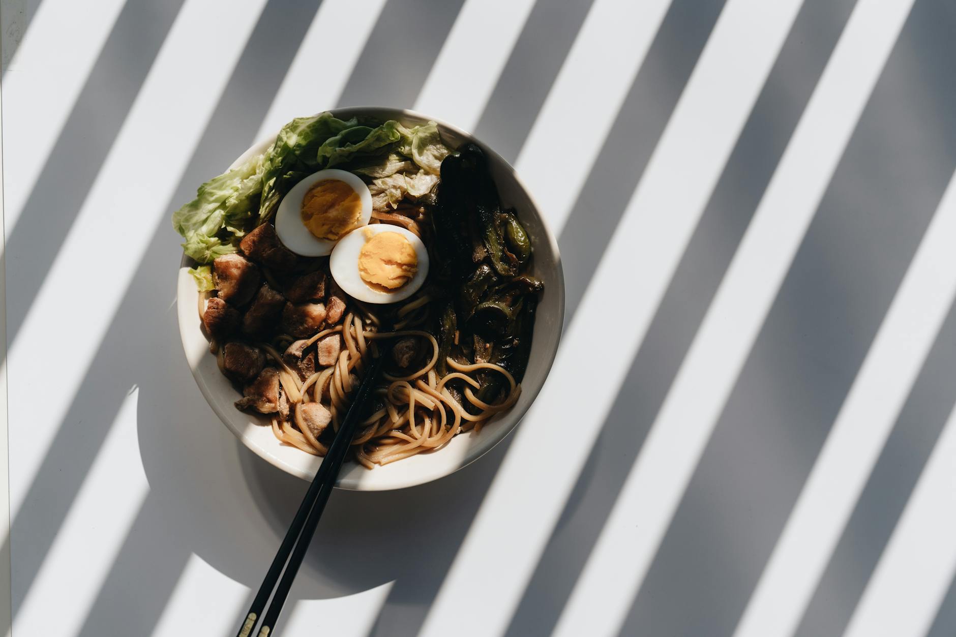 Miska ramenu z jajkiem, mięsem i zieleniną w mocnym świetle i cieniu