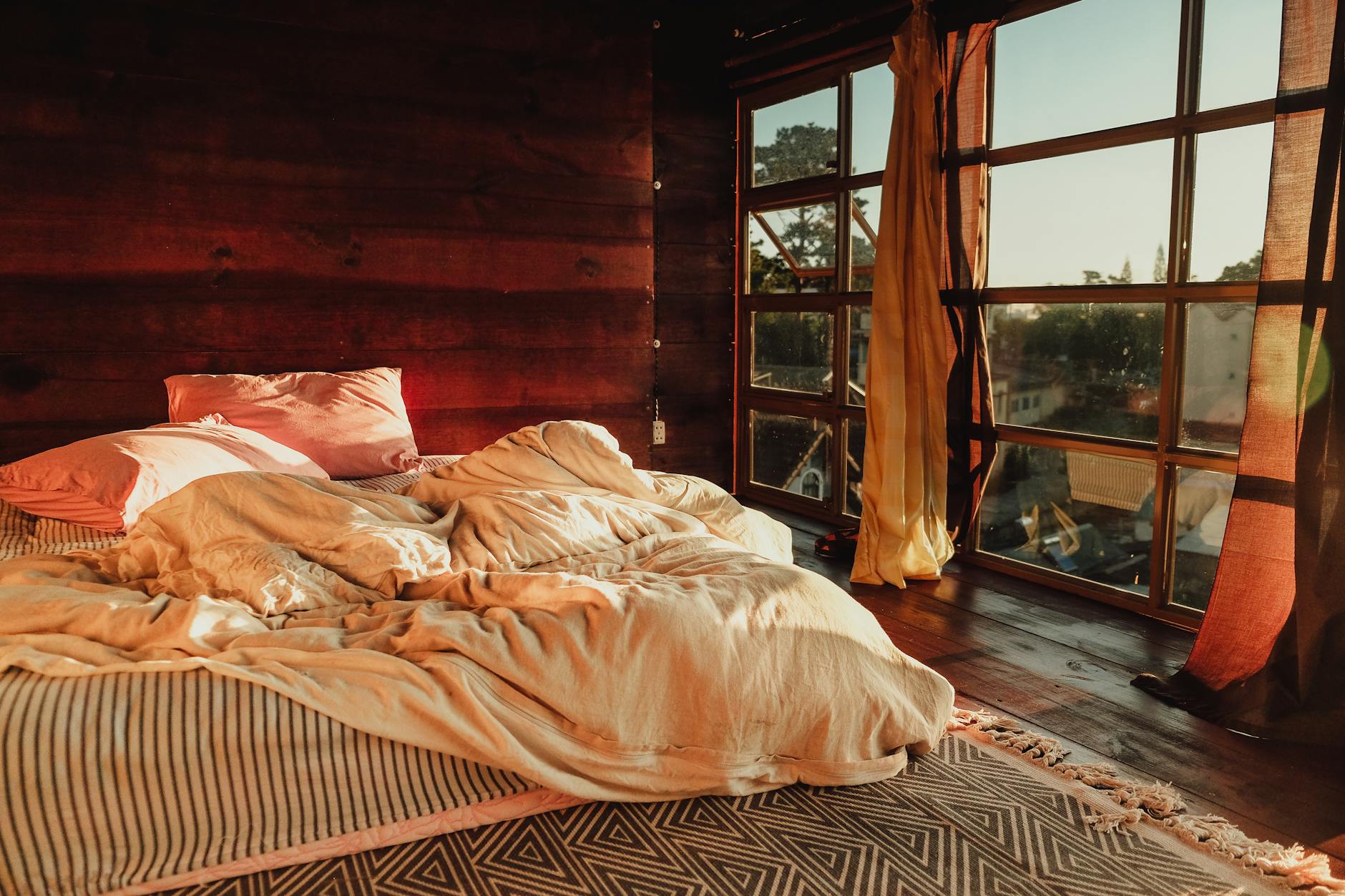 Sypialnia z niepościelonym łóżkiem w porannym słońcu zza dużych okien