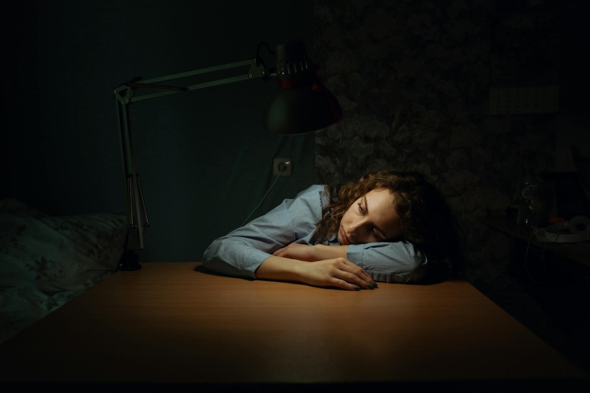 5 składników, które najczęściej kradną Ci energię w ciągu dnia Zmęczona kobieta opiera głowę na biurku przy lampce w ciemnym pokoju
