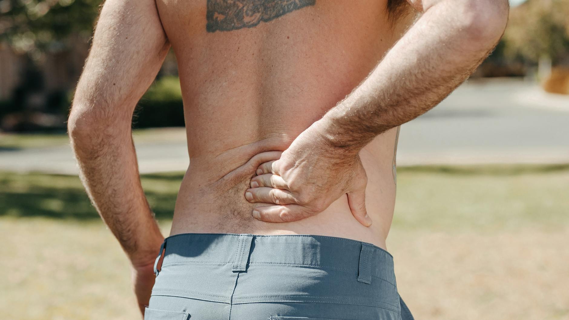 Jeśli bolą plecy po treningu: jak odróżnić zakwasy od przeciążenia i co zmienić Mężczyzna bez koszulki trzyma bolące lędźwie po treningu na dworze