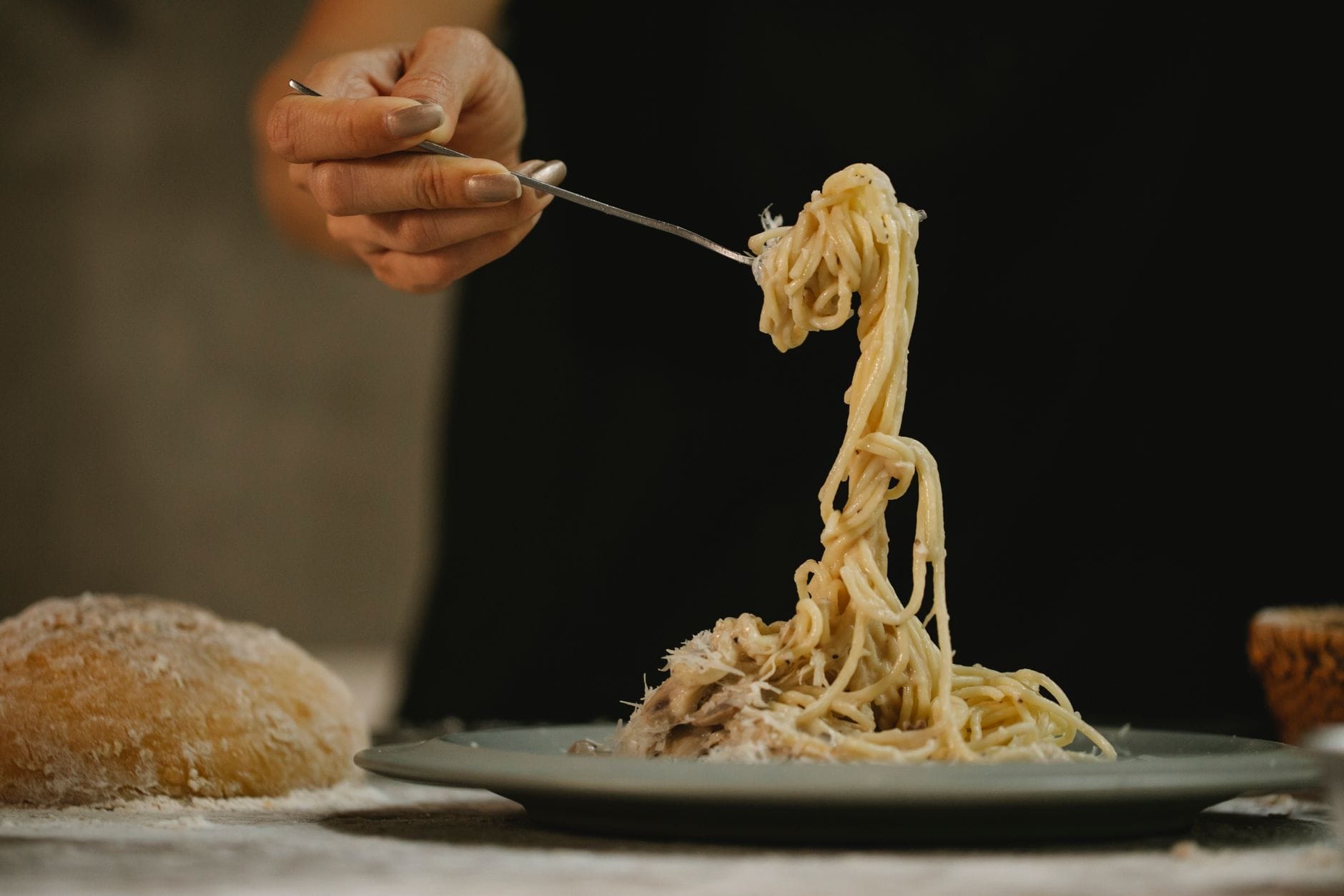 Kobieta je spaghetti w kremowym sosie grzybowym przy chlebie na stole