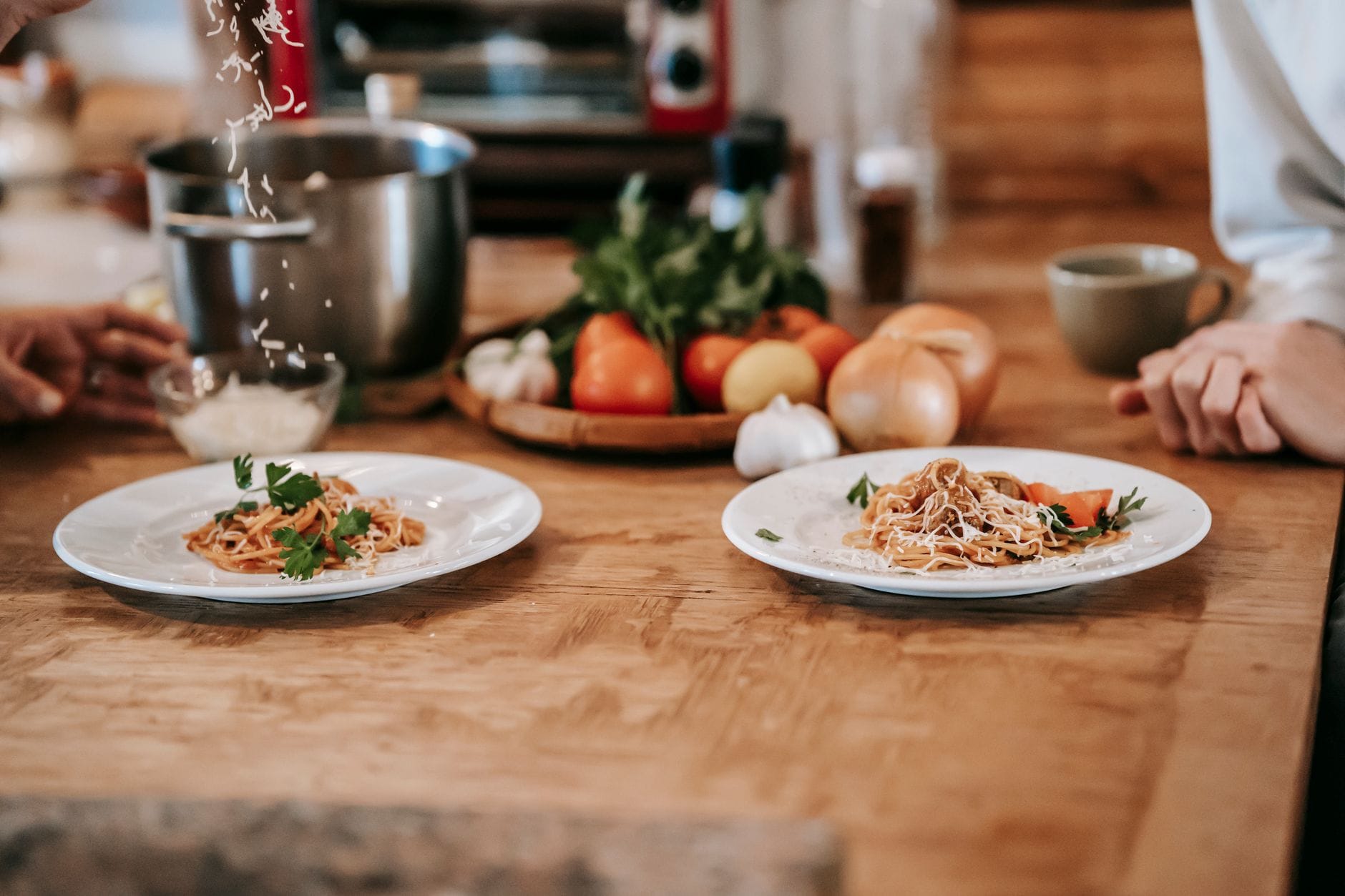 Kobieta posypuje domowe spaghetti tartym serem przy stole z mężem