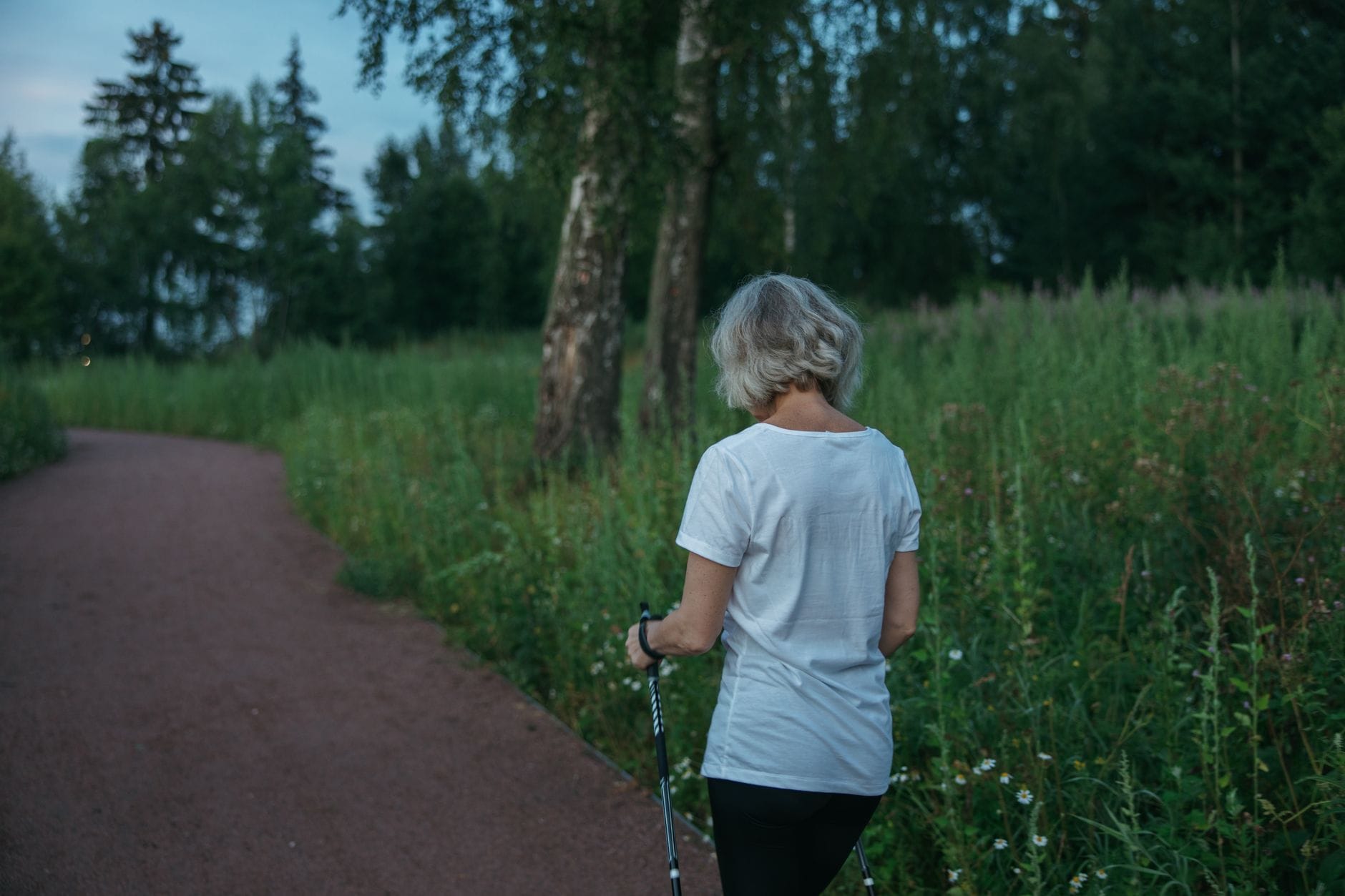 Starsza kobieta z kijkami nordic walking spaceruje po parku