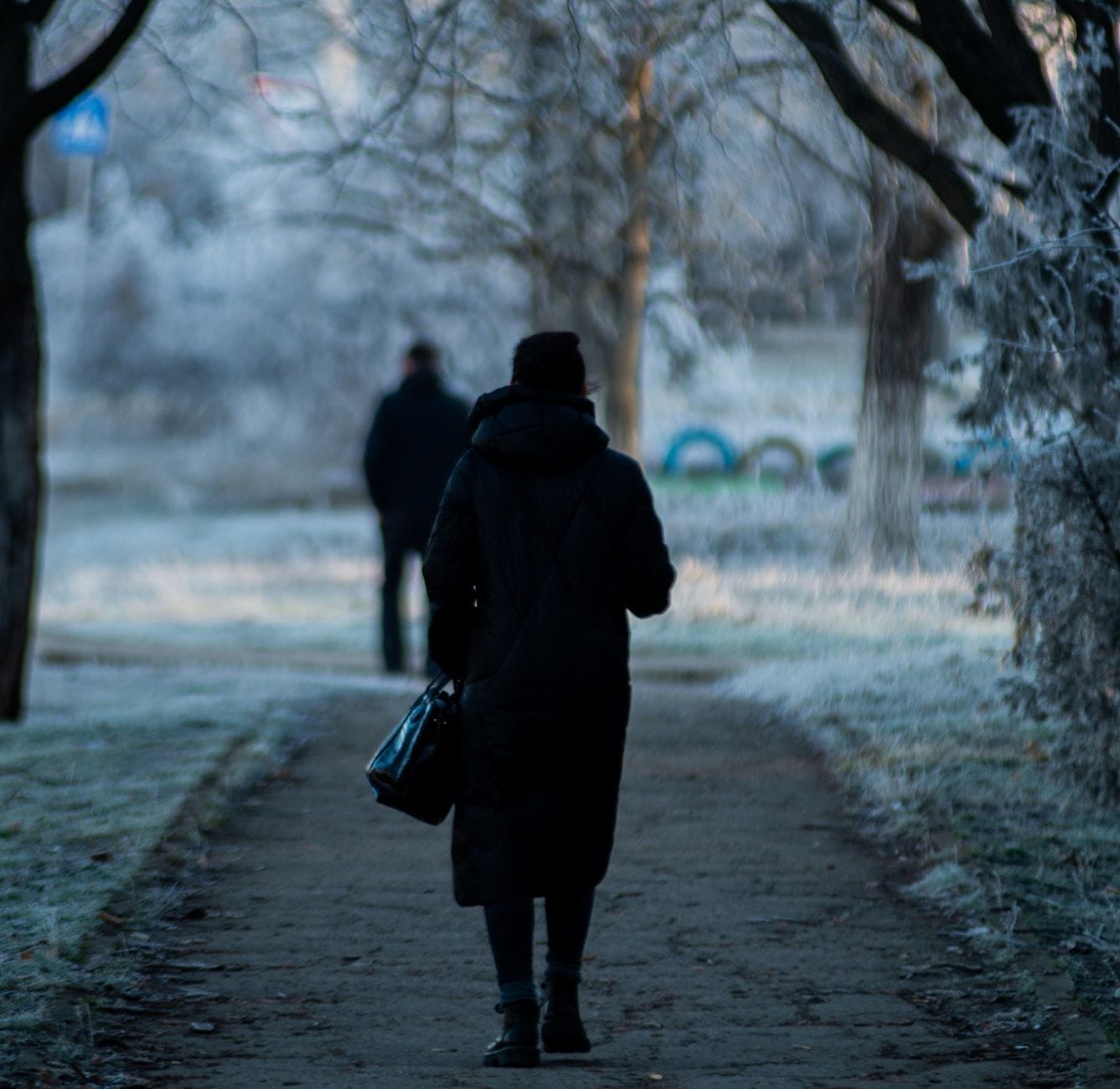 Sylwetki ludzi idących zimą po ośnieżonym parku miejskim