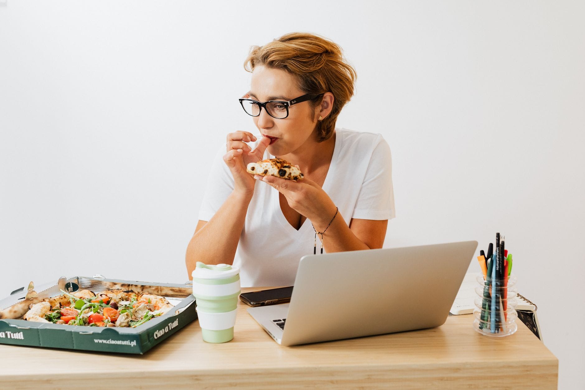 Dlaczego czujesz zmęczenie mimo jedzenia „zdrowo”? 9 częstych pułapek Kobieta je pizzę przy biurku, pracując na laptopie